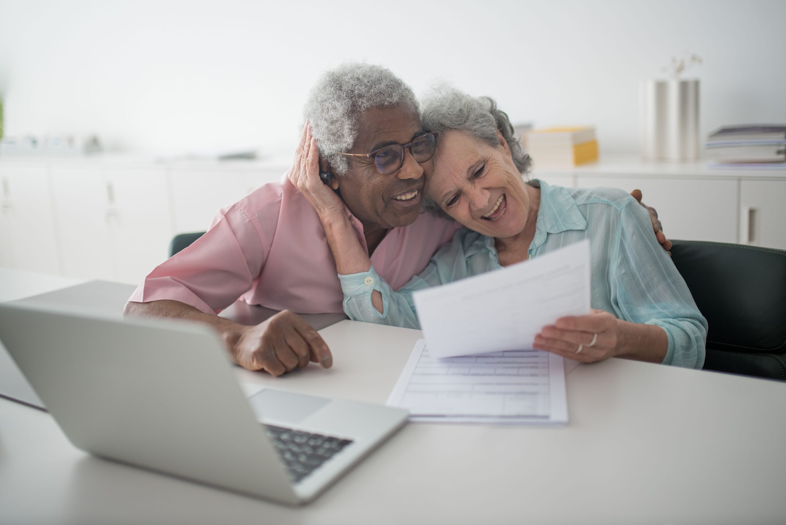Home A joyful senior couple smiling while reviewing documents together at a desk with a laptop.